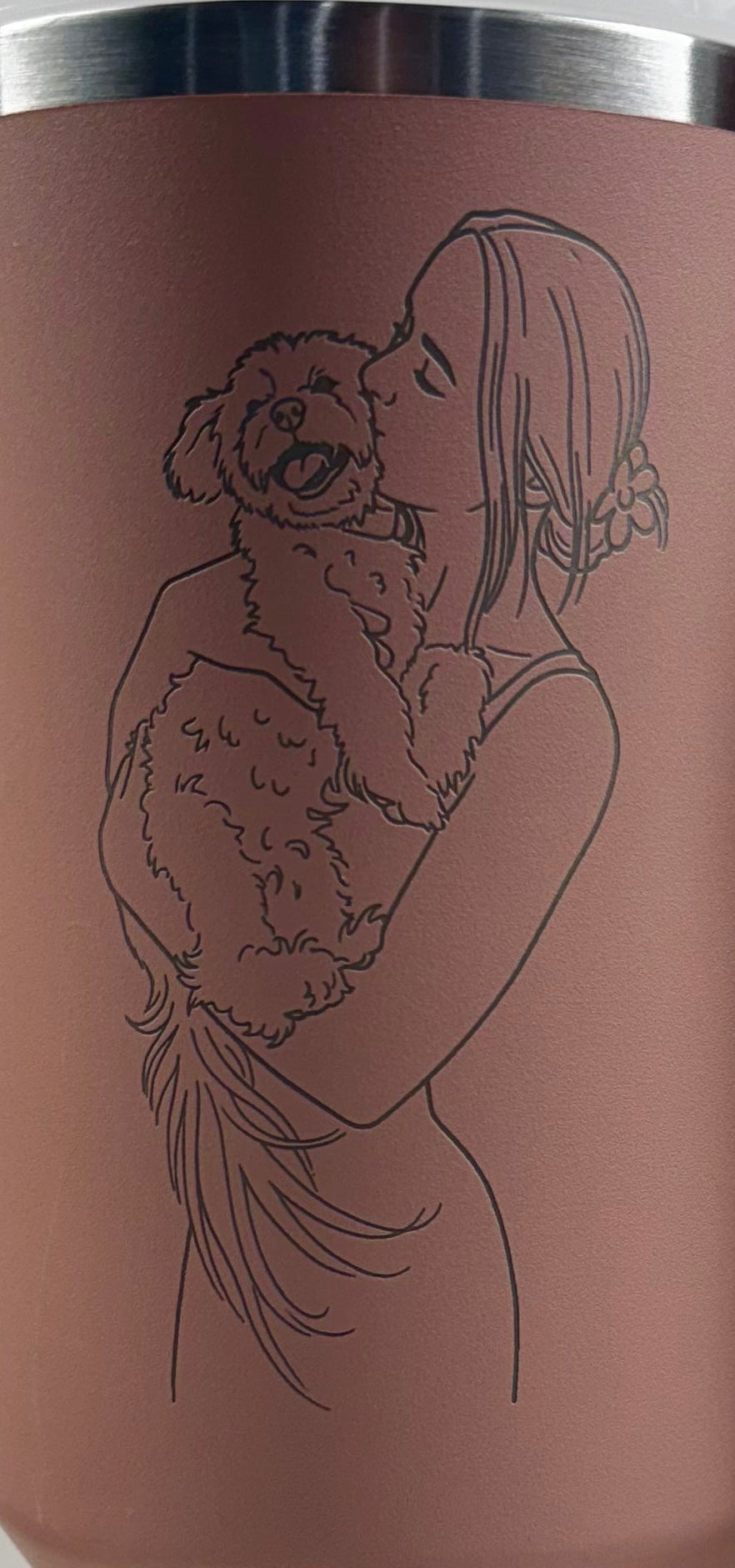 Pink travel mug with a engraved design of a couple hugging on a white surface.